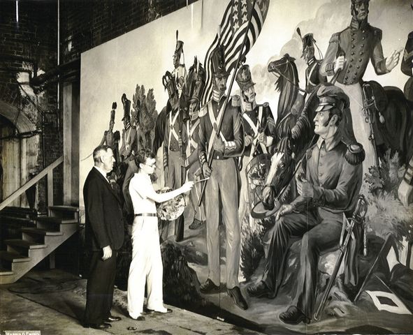 photo of mural labeled 'General Frank C. Burnett, Director of Exhibits for the War Department inspects a section of the big mural being painted by Kenneth Stubbs.